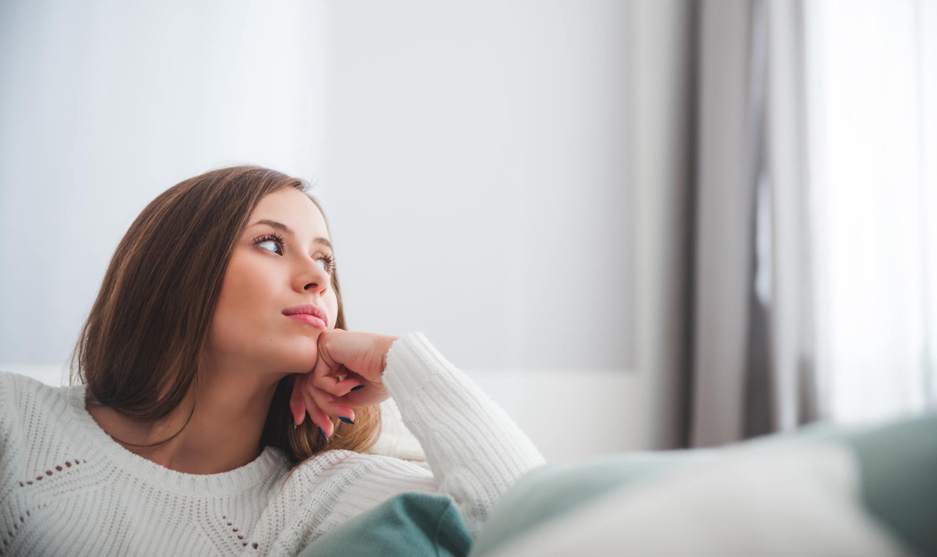 A girl in a white sweater is sitting on the sofa and thinking about OTP life insurance